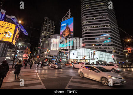 TORONTO, ONTARIO - NOVEMBER 13, 2018: Skyscrapers on Yonge Dundas Square, with people crossing on a sidewalk at night , stores and shops, in a typical Stock Photo