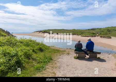 Older couple sitting on a bench enjoying the view of Broad Haven beach on the Pembrokeshire coast, Wales Stock Photo