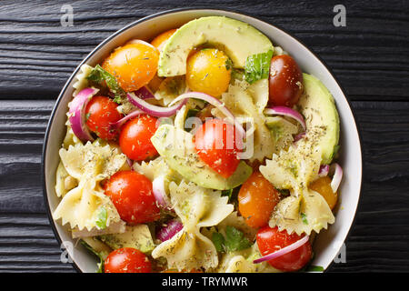 Appetizer Farfalle pasta salad with ripe avocado, onion and tomato closeup in a bowl on the table. Horizontal top view from above Stock Photo