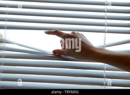 Female hand separating slats of venetian blinds with a finger to see through Stock Photo