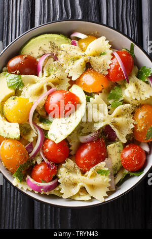 Italian pasta salad farfalle with ripe avocado, onions and tomatoes closeup in a bowl on the table. Vertical top view from above Stock Photo