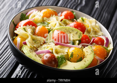 Pasta farfalle with ripe avocado, onions and tomatoes with spicy sauce closeup in a bowl on the table. horizontal Stock Photo
