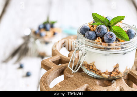 Healthy breakfast of blueberry parfaits made with fresh fruit, Greek yogurt, granola and mint leaves over a rustic cake stand.  Selective focus. Stock Photo