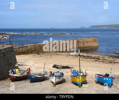 A colorful array of boats hauled up on to the quay at Sennen Cove, Cornwall, England, with a view of the harbour wall and sea behind. Stock Photo