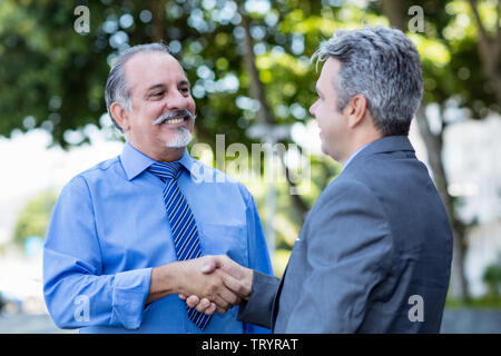Handshake of senior businessman and mature man in suit outdoor in the city Stock Photo