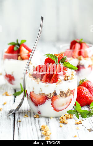 Healthy breakfast of strawberry parfaits made with fresh fruit, yogurt and granola over a rustic white table. Selective focus. Stock Photo