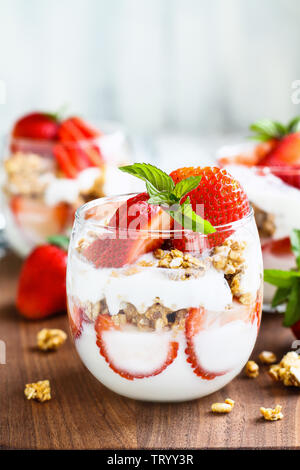 Healthy breakfast of strawberry parfaits made with fresh fruit, yogurt and granola over a rustic wood table. Selective focus. Stock Photo
