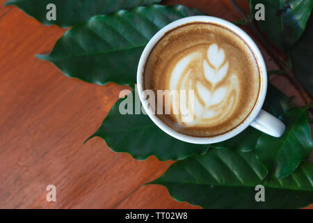 White coffee mugs and coffee beans Poured on a wooden table, beautifully arranged, decorated with coffee leaves. Is a mixture of raw materials for mak Stock Photo