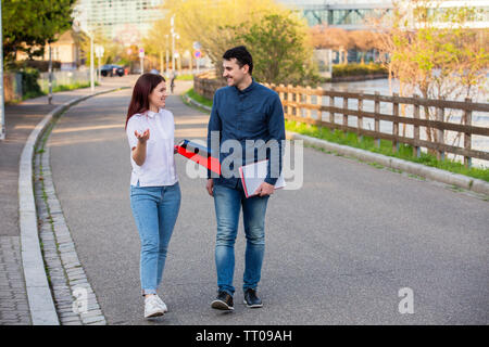 Young students smiling and speaking to each other in the city while taking a walk. Young students outdoors taking a break from studying on a city stre Stock Photo