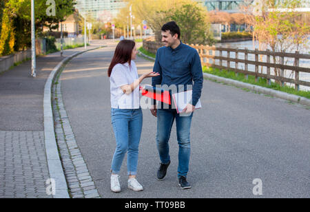 Young students smiling and speaking to each other in the city while taking a walk. Young students outdoors taking a break from studying on a city stre Stock Photo