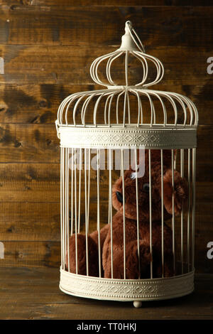 Toy bear in decorative cage  on wooden background Stock Photo