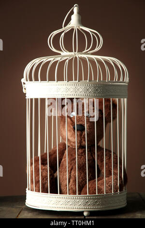Toy bear in decorative cage on wooden table, on brown background Stock Photo