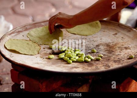 a mexican woman cooking tortillas on a mexican three stone stove fired by wood and broad beans, rural scene Stock Photo