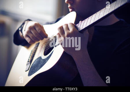 A professional musician in black clothes plays his favorite acoustic six-string guitar, holding the fretboard at the base and sitting in the twilight. Stock Photo