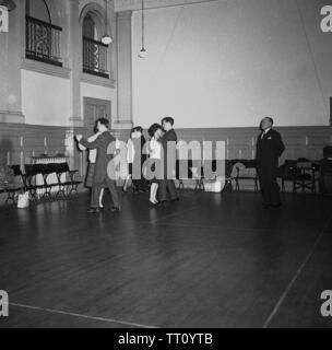 1950s, historical, evening time and three couples at a ballroom dancing class, England, UK, whose movements are being watched by a male teacher. In this post-war era before mass television and home entertainment, educational evening classes such as learning ballroom dance were popular social activities for the adult population. Stock Photo