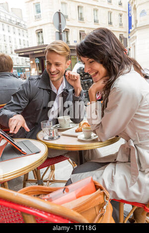 Happy, smiling man and woman couple sitting at sidewalk cafe looking at tablet computer using wireless technology outdoors, Paris, France Stock Photo
