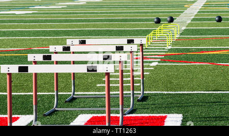 Hurdles and medicine balls are set up on a turf field for speed work training of high school athletes. Stock Photo