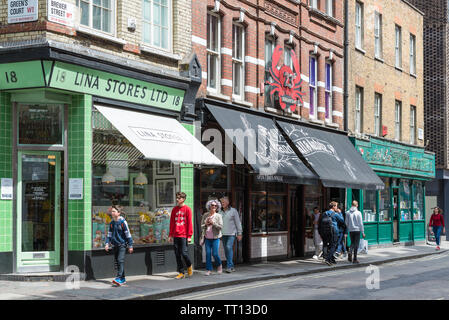 Groups of people walking past the Lina Stores, Randall and Aubin restaurant and Soho Original Books shop in Brewer Street, Soho, London Stock Photo