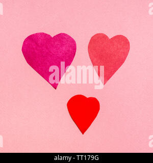 three various hearts cut from red papers on pink paper background Stock Photo