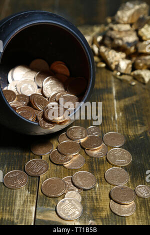 Golden coins falling out from pot, on wooden background Stock Photo