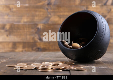 Golden coins falling out from pot, on wooden background Stock Photo