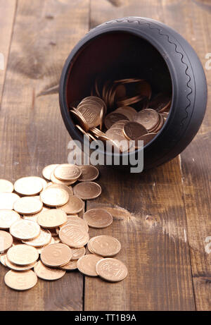 Golden coins falling out from pot, on wooden background Stock Photo