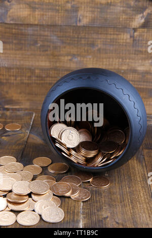 Golden coins falling out from pot, on wooden background Stock Photo