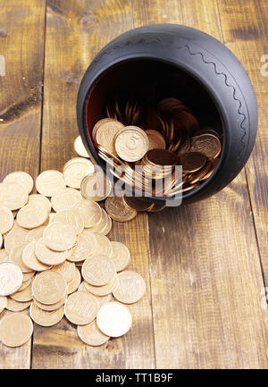 Golden coins falling out from pot, on wooden background Stock Photo