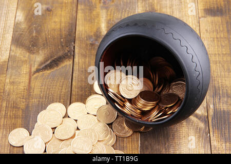 Golden coins falling out from pot, on wooden background Stock Photo