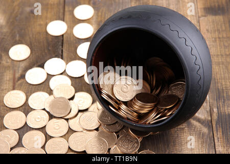 Golden coins falling out from pot, on wooden background Stock Photo