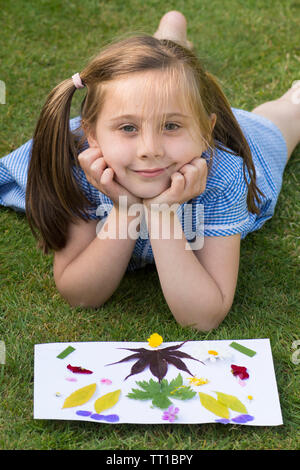 eight year old girl in school uniform dress after school, in garden, posing by a picture made from flowers and leaves stuck on paper, nature art craft Stock Photo