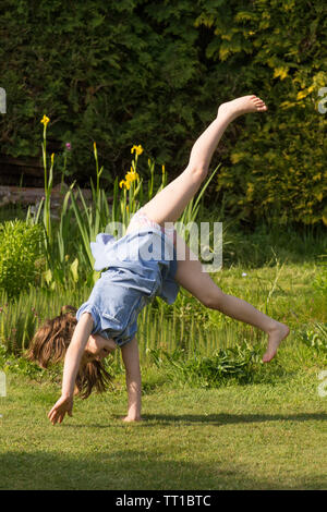 eight year old girl doing cartwheels in school uniform dress after school in garden practicing gymnastics Stock Photo