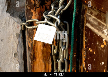 Steel chain with a padlock securing a wooden door shut on a wooden post in Granada, Spain. Stock Photo