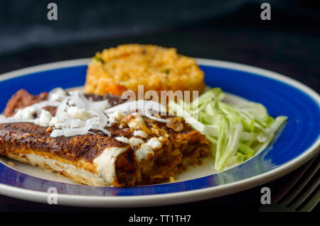 Mexican enmoladas, enchiladas topped with mole sauce and queso fresco, served with rice and salad. Isolated on dark background with copy space Stock Photo