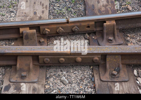 Close-up detail of links between hot rolled steel railway track sections and fasteners, sleepers and ballast at Didcot Railway Centre, Oxfordshire, UK
