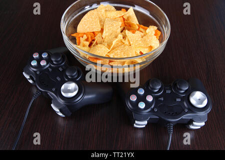 Black game controllers and bowl with snacks on wooden background Stock Photo