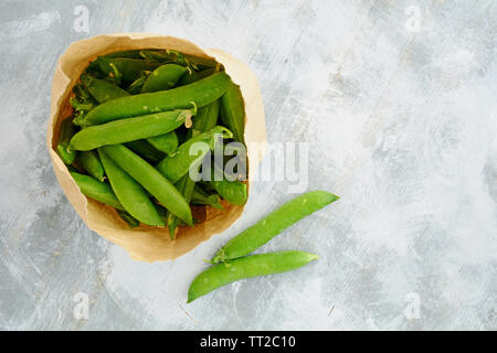 Fresh from the garden organic English peas in brown paper bag on rustic wooden background.  In flat lay composition, horizontal format with room for t Stock Photo