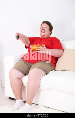 Lazy overweight male sitting on couch and watching television Stock Photo