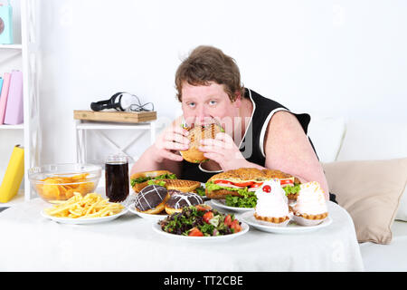 Fat man eating a lot of unhealthy food, on home interior background Stock Photo