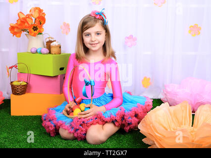 Beautiful small girl in petty skirt holding basket with colorful eggs on decorative background Stock Photo