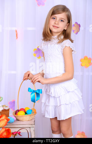 Beautiful small girl holding basket with colorful eggs on decorative background Stock Photo