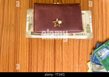 Five hundred (500) cash note in brown ladies purse and stack of credit cards on a wooden table. Business finance economy concept. High angel view with Stock Photo