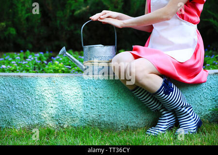 Young woman in rubber boots holding watering can, outdoors Stock Photo