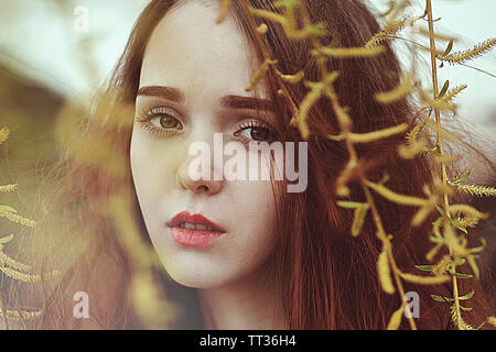 Portrait of a romantic girl with red long hair in the wind under a willow tree. Stock Photo