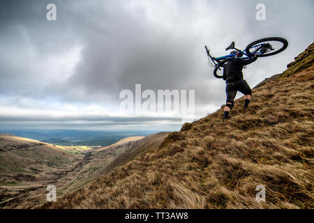 A man carries a mountain bike on his shoulders to the summit of Fan-y-Big in the Brecon Beacons National Park, Wales. Stock Photo