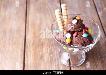 Chocolate ice cream with multicolor candies and wafer rolls in glass bowl, on wooden background Stock Photo