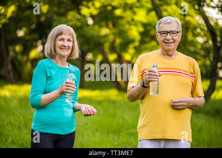 Happy senior couple is drinking water after exercising in park. Stock Photo