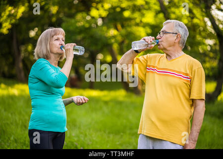 Happy senior couple is drinking water after exercising in park. Stock Photo