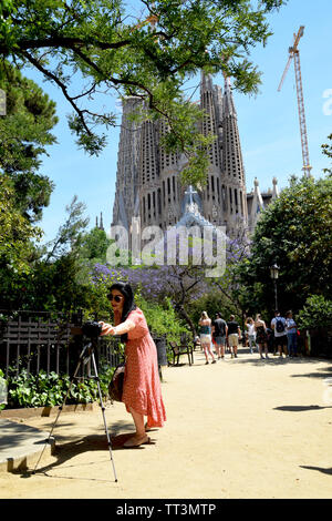 Young woman fixing the settings on her camera, in order to get ready to take photos of her in front of famous cathedral Sagrada Familia in Barcelona Stock Photo