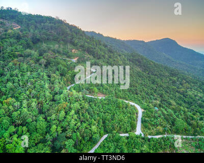 Aerial view of curvy mountain road through a jungle ay sunset